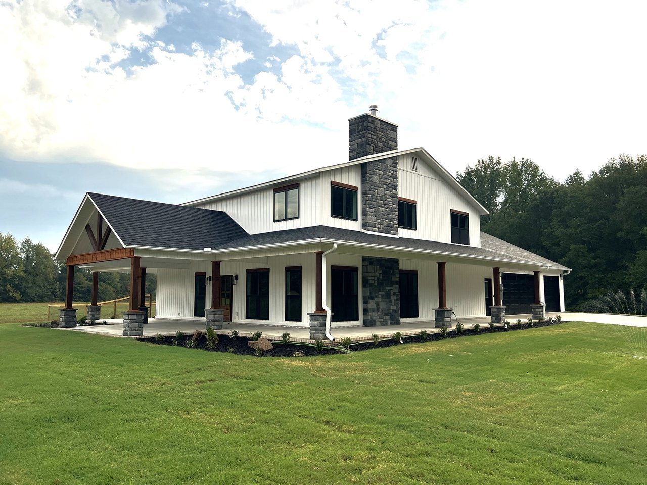 The Crawford, a white farmhouse with a wraparound porch, timber accents, and a green lawn