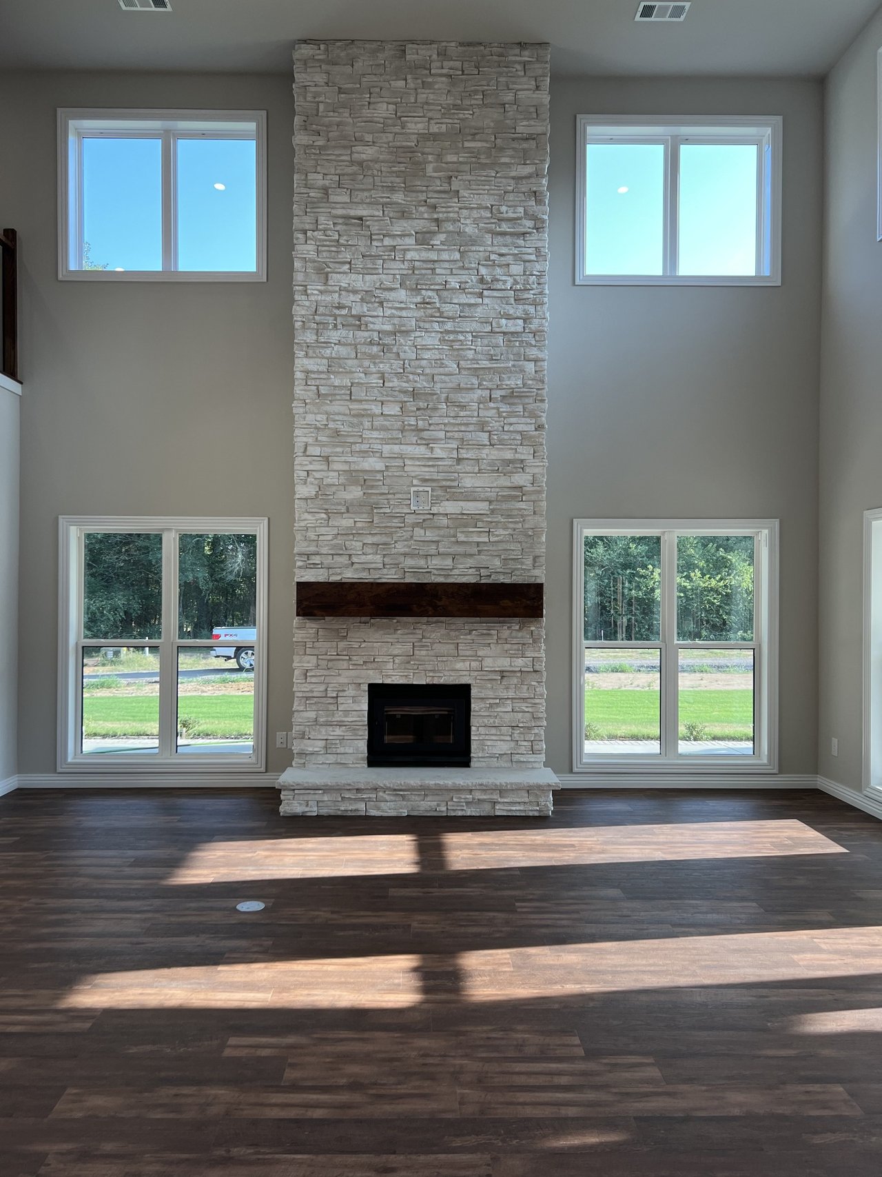 Double-height living room with a tall stone fireplace and sunlit windows